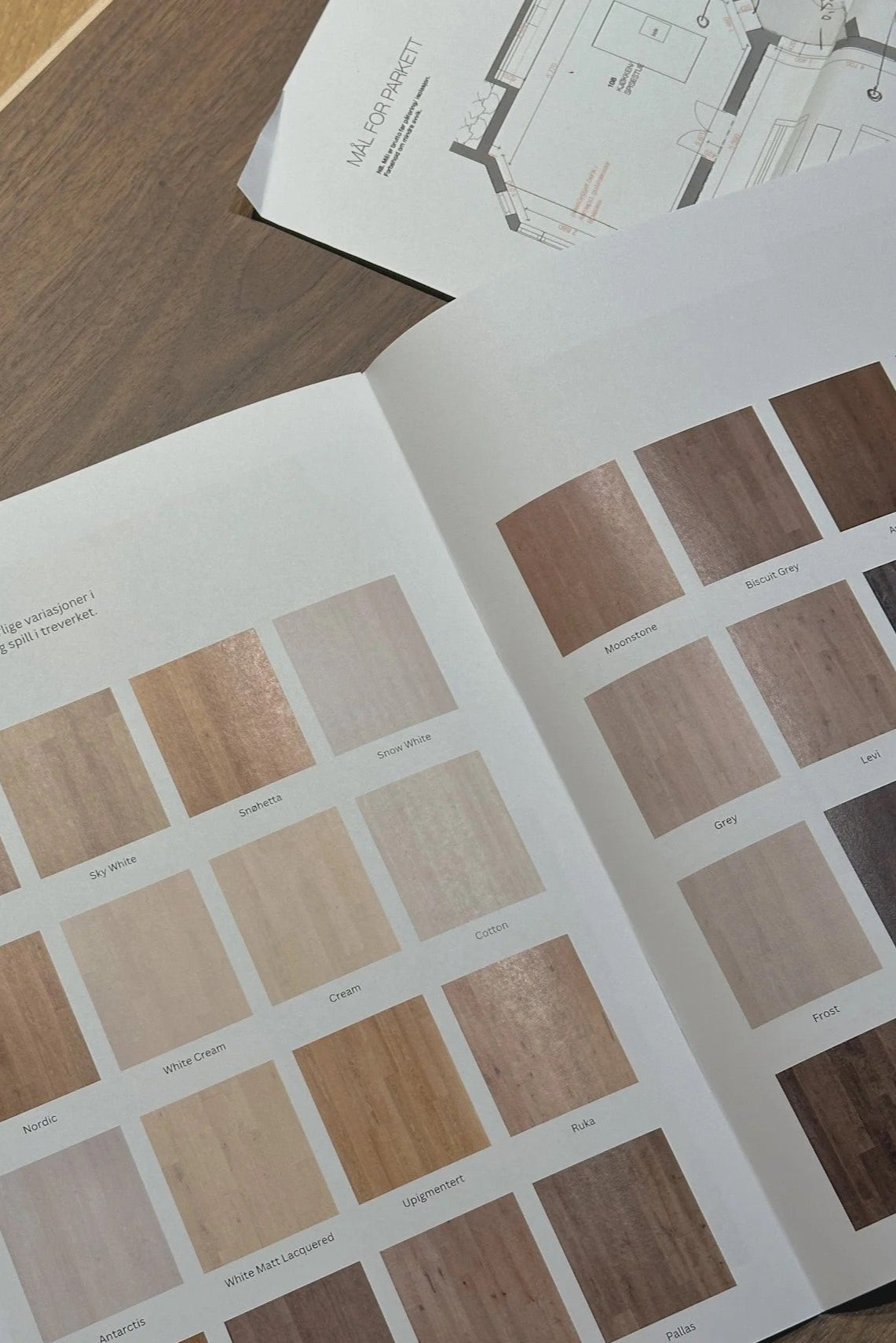 Wood color swatch book open on a wooden surface with architectural plans in the background