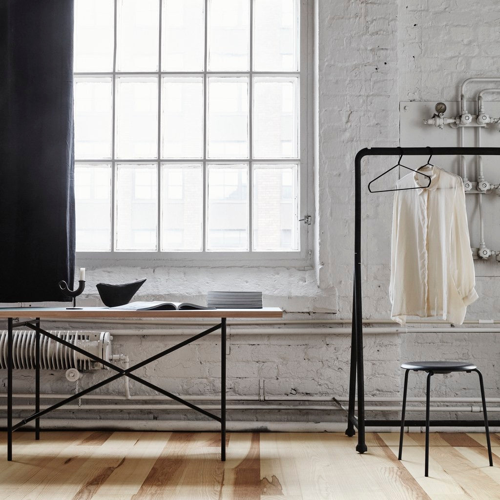 Modern interior with a ash wooden flooring, a large window, black metal clothing rack, and white brick wall.