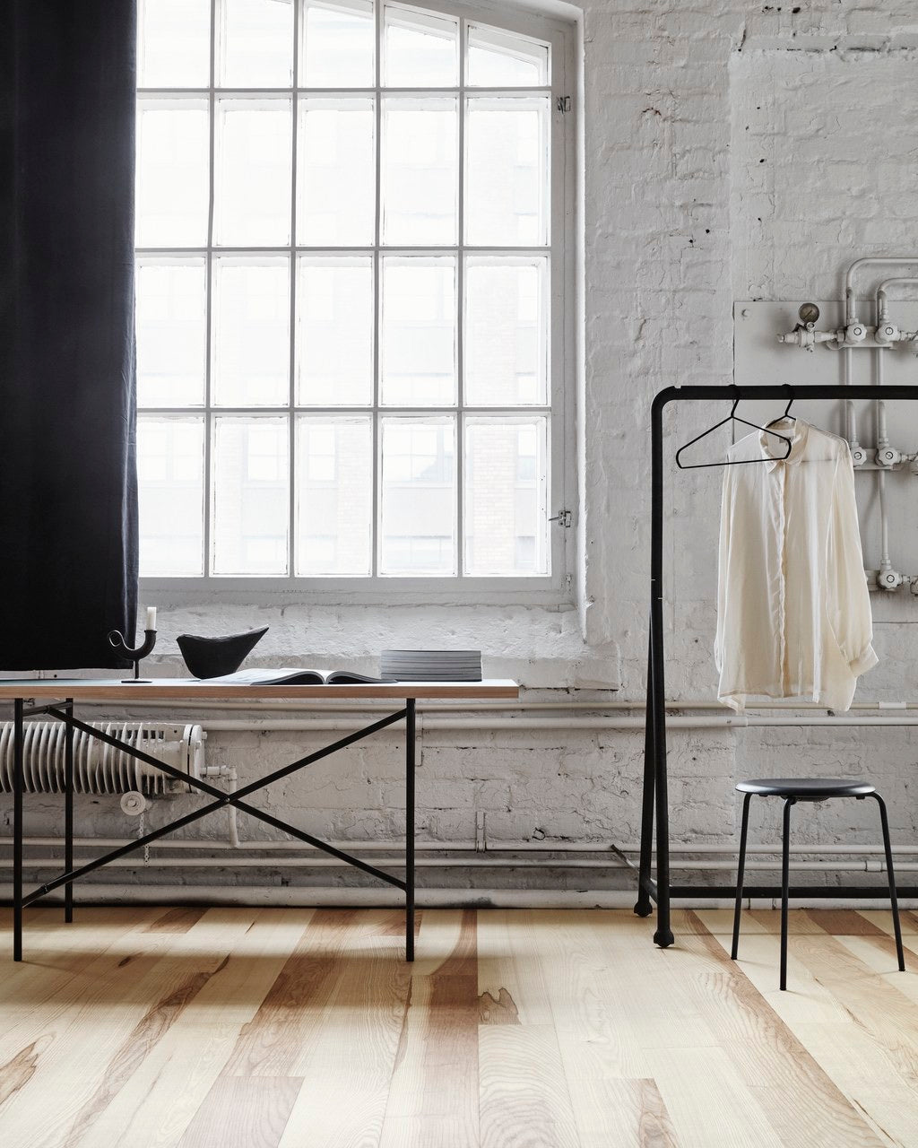 Modern interior with a ash wooden flooring, a large window, black metal clothing rack, and white brick wall.